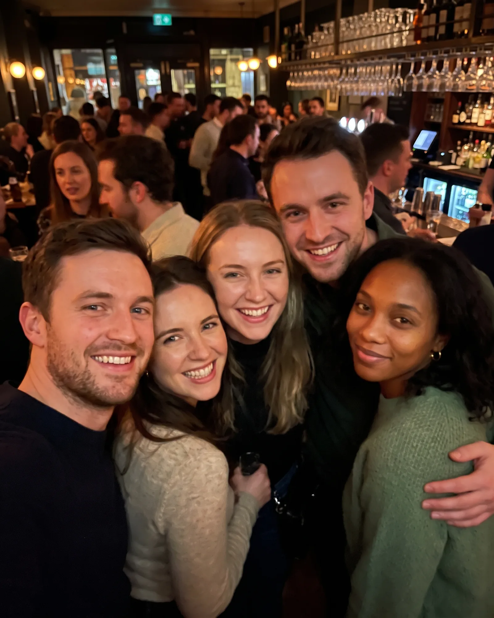 The same woman squeezed in at the far right of a five-person group photo in a busy bar.