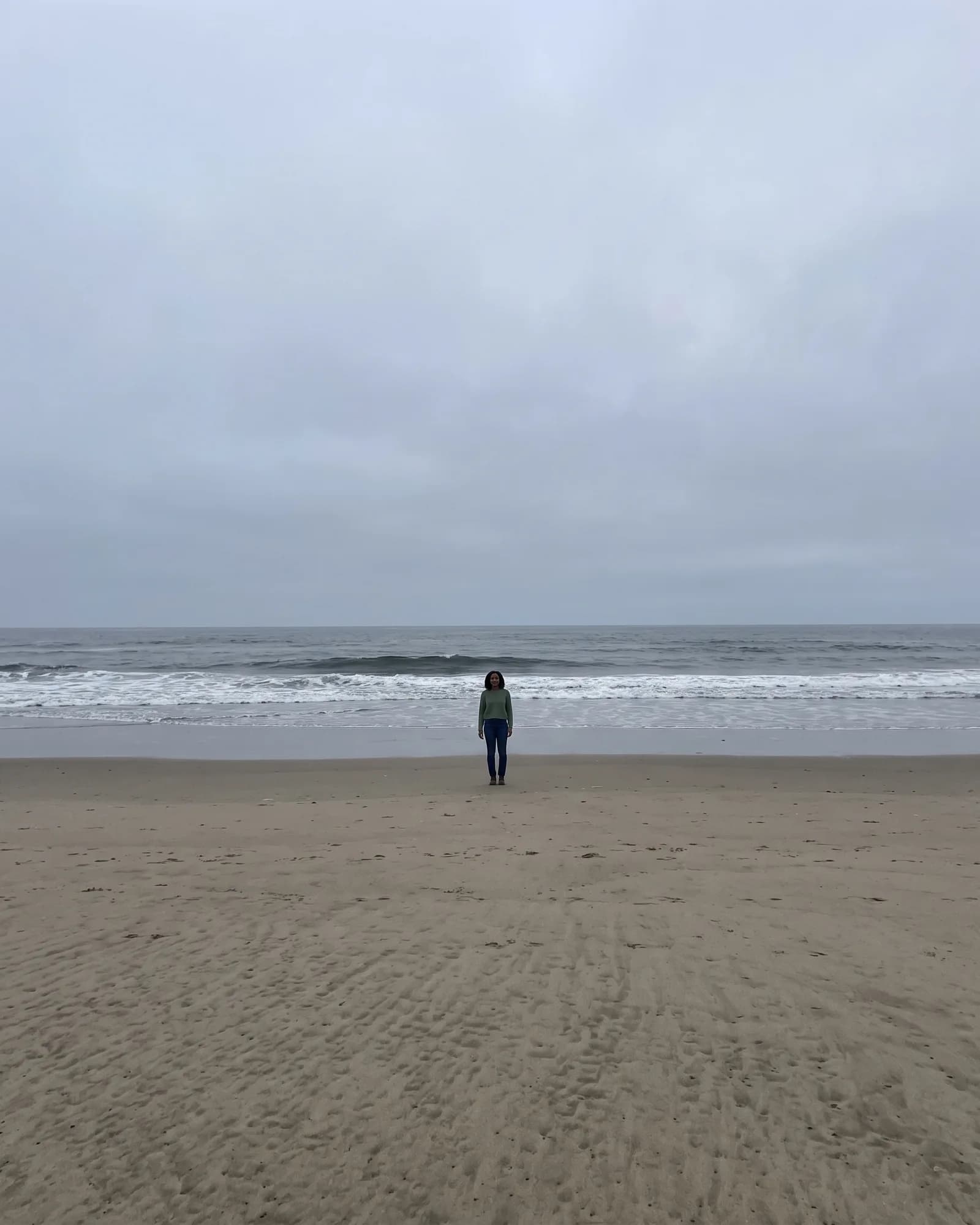 The same woman standing far off on a beach so her face is tiny in the frame.